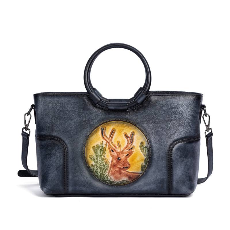Sac en cuir bleu avec anses rondes, orné d’un médaillon illustrant un cerf stylisé, représentant le modèle Cervus Heritage