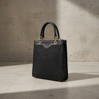 Sac vertical en cuir véritable et raphia noir, avec fermeture zippée, poignées renforcées, attache dorée, poche intérieure zippée et bandoulière amovible et réglable.