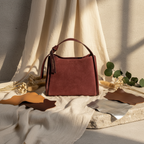 Sac Alice en cuir suédé bordeaux avec insertions en cuir grainé dollar, silhouette trapèze structurée et accessoires dorés brillants, fabriqué en Italie.